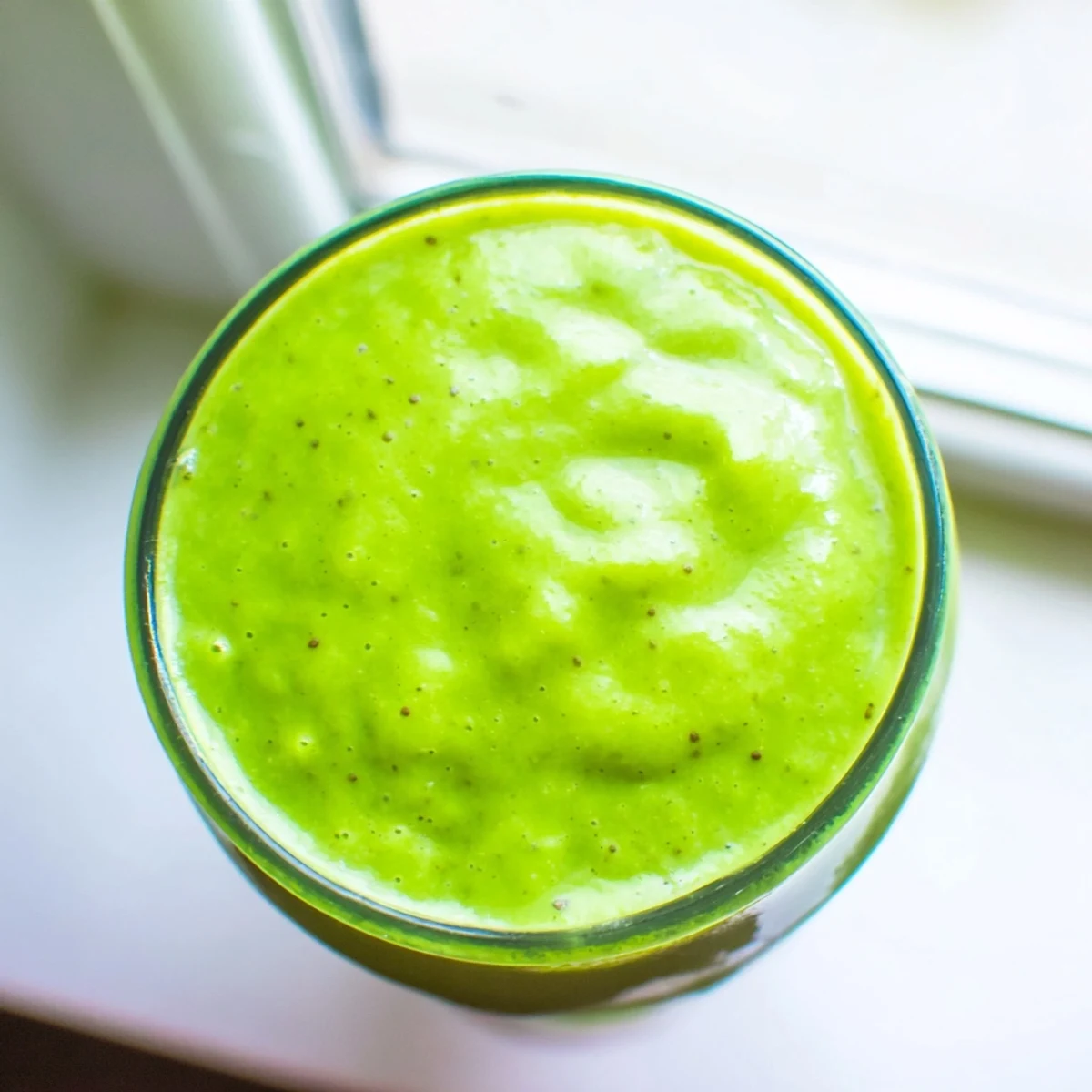 Creamy green spinach-hidden smoothie in tall glasses garnished with fresh mango and pineapple chunks.  