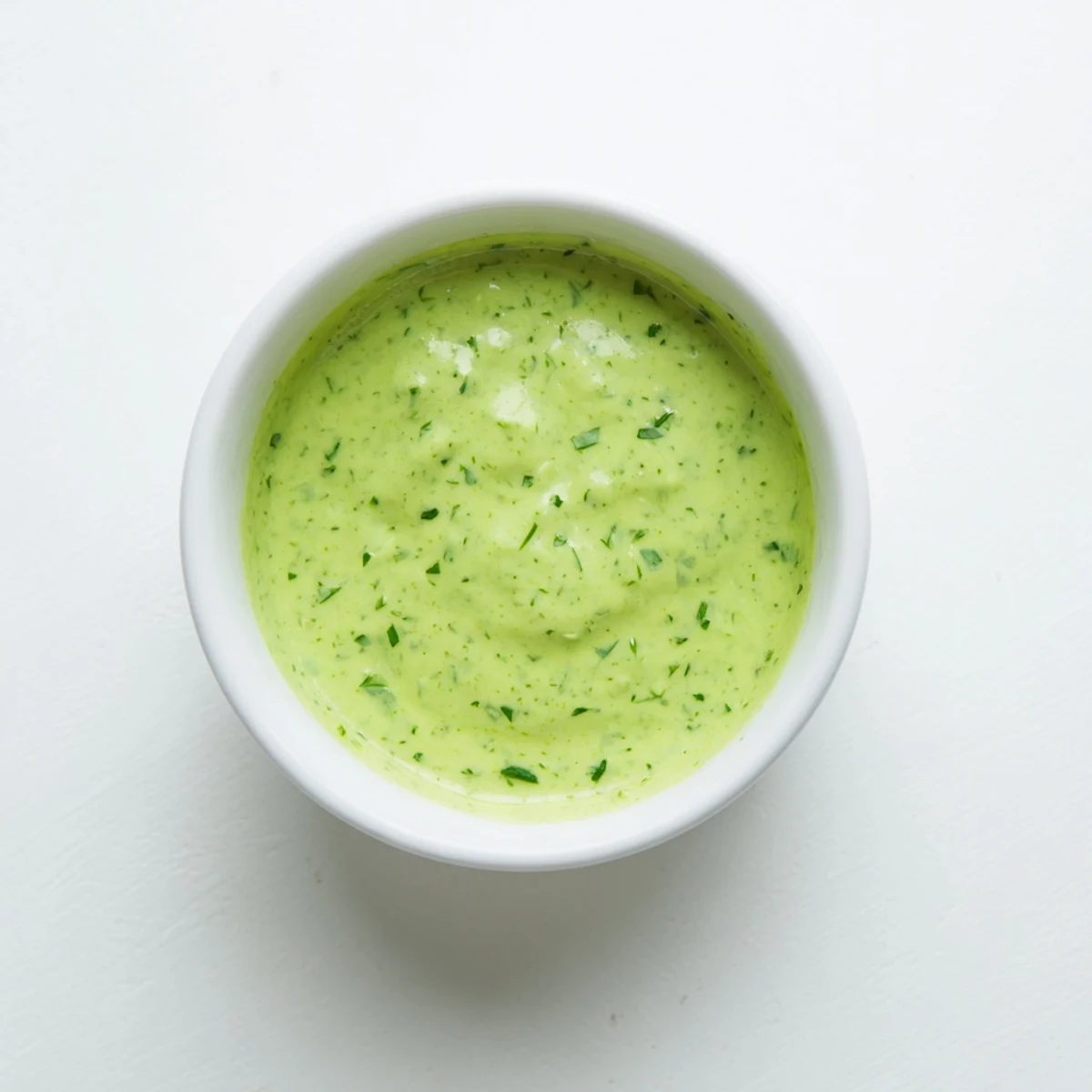 Spoon dipping into creamy Green Goddess Dressing, with visible flecks of parsley and tarragon in a rustic ceramic bowl.