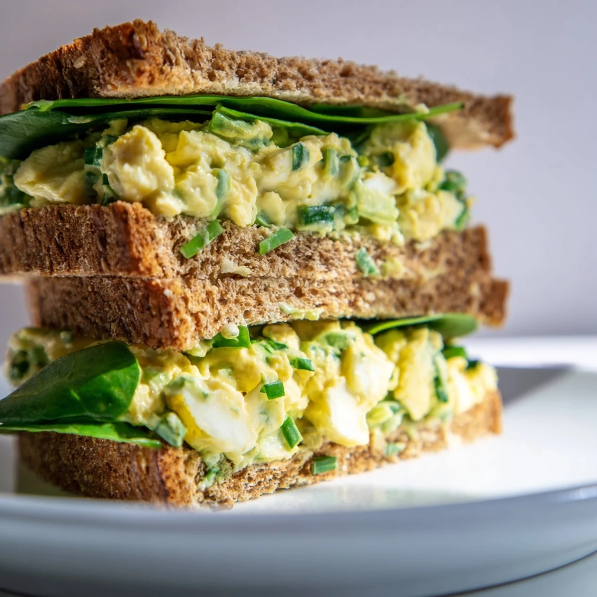 Close-up of a vibrant Avocado Egg Salad Sandwich on whole grain bread, with creamy green filling and fresh chives.