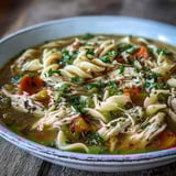 A cozy bowl of Chicken and Noodle Soup featuring hearty vegetables and soft egg noodles in a rich broth, served with a lemon wedge and crusty bread on the side.  