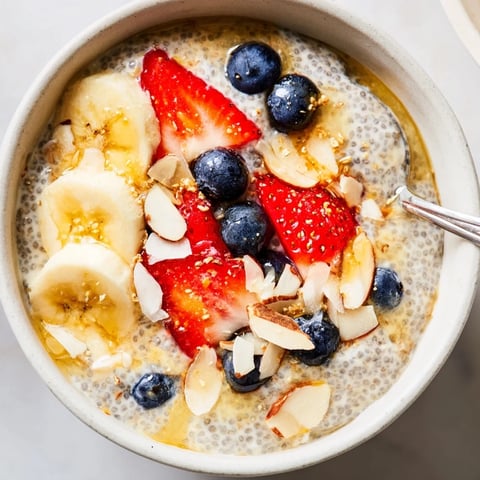 Creamy overnight chia seed pudding in a glass jar, topped with fresh mixed berries, sliced almonds, and shredded coconut for a healthy breakfast.