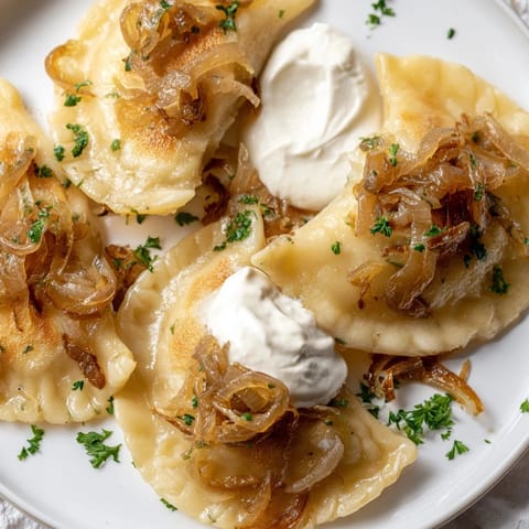 Warm, comforting image of pan-fried Polish pierogi, served with sweet caramelized onions and sour cream.