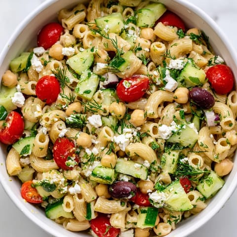 A vibrant bowl of Lemon Herb Chickpea Pasta Salad, featuring diced vegetables, fresh dill, and mint on a rustic wooden table.