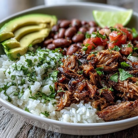 Steaming carnitas bowl with fluffy rice, pinto beans, and creamy avocado slices topped with fresh pico de gallo.  