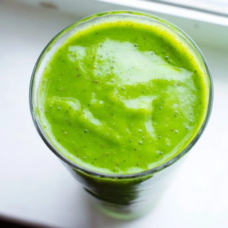 Refreshing spinach-hidden smoothie poured from blender into glasses, showing vibrant green hue and frothy texture.  
