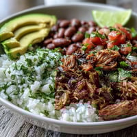 Steaming carnitas bowl with fluffy rice, pinto beans, and creamy avocado slices topped with fresh pico de gallo.  